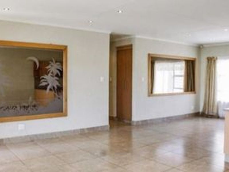 Spacious open-plan living area featuring neutral tiled flooring, recessed downlighting, and decorative wall mirrors, offering a versatile layout for modern living.