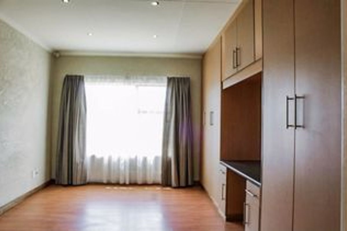 A bright, empty bedroom featuring laminate flooring, recessed downlights, and extensive built-in cupboard storage.