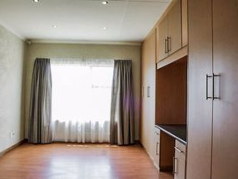 A bright, empty bedroom featuring laminate flooring, recessed downlights, and extensive built-in cupboard storage.