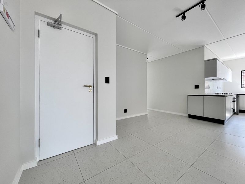 Modern open-plan living area featuring sleek tiled floors, track lighting, and a contemporary kitchen with built-in cabinetry and integrated appliances.
