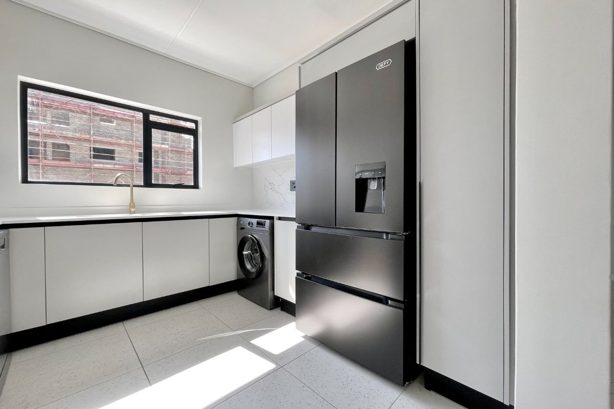 Modern scullery featuring sleek white cabinetry, stone countertops, brass fixtures, and integrated appliances, providing a clean and functional utility space.