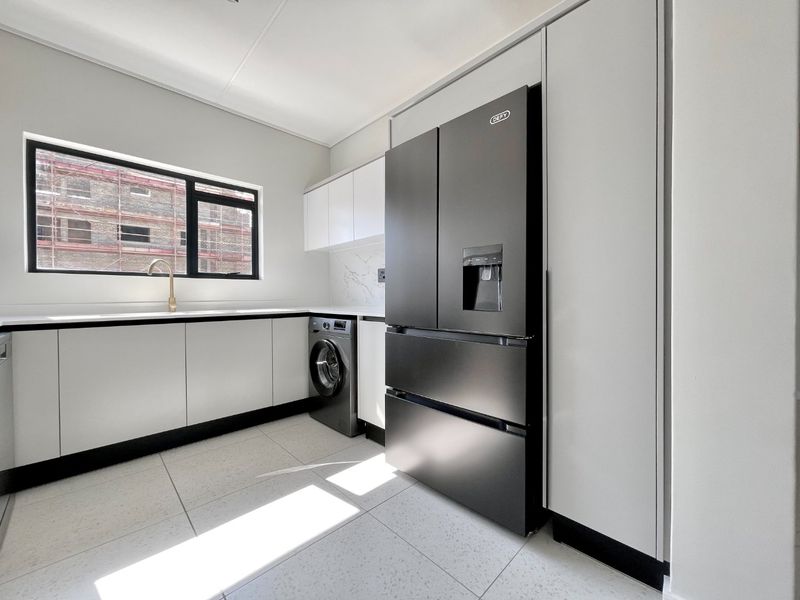 Modern scullery featuring sleek white cabinetry, stone countertops, brass fixtures, and integrated appliances, providing a clean and functional utility space.