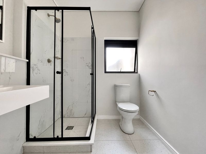 Modern bathroom featuring a glass-enclosed shower with marble-look tiles, a wall-mounted basin, and a toilet, finished with neutral floor tiles.