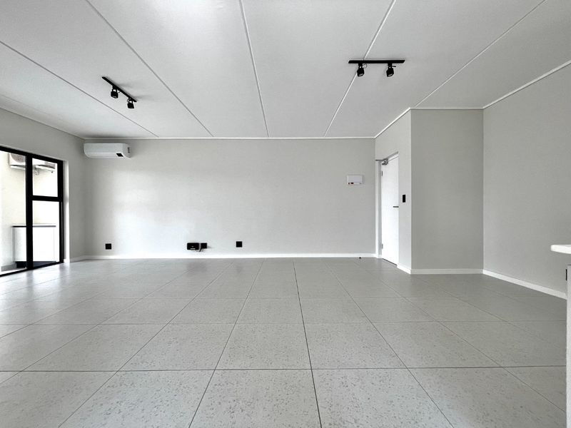 A spacious, modern open-plan living area featuring neutral tiled flooring, track lighting, and a wall-mounted air conditioning unit.