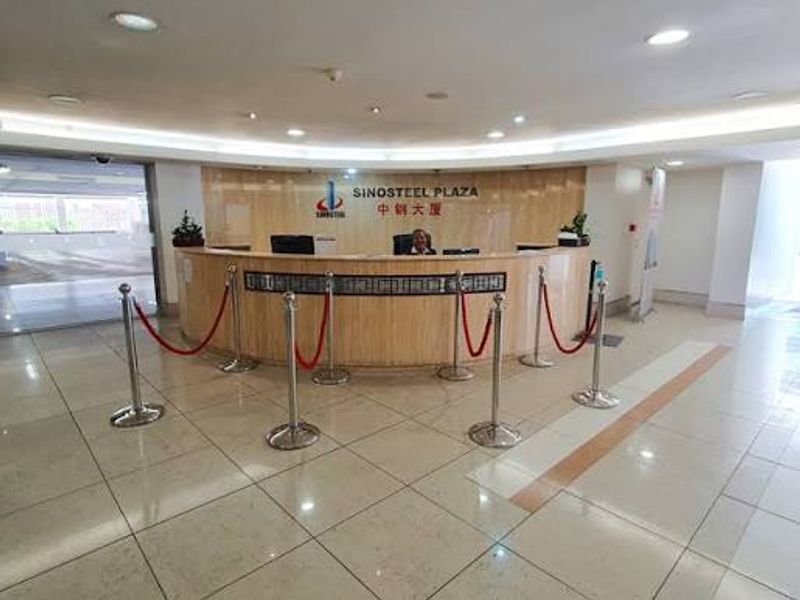 A professional commercial building reception area featuring a curved wooden reception desk, polished tiled flooring, and modern recessed cove lighting.