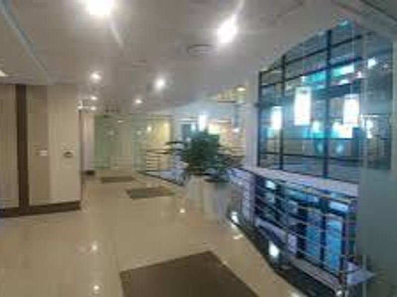 A spacious commercial hallway featuring polished tiled flooring, modern glass partitions, and recessed ceiling lighting, providing a professional and well-lit circulation area.
