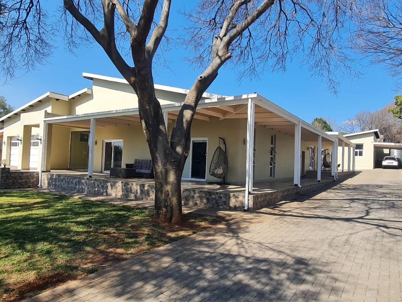 A spacious single-story home featuring a large covered patio, stone-clad base, and an extensive paved driveway leading to a garage.