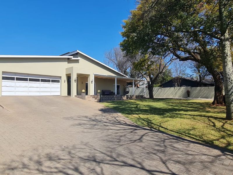Front view of a residential property featuring a paved driveway, attached carport, garage, and a covered patio area set within a landscaped garden.