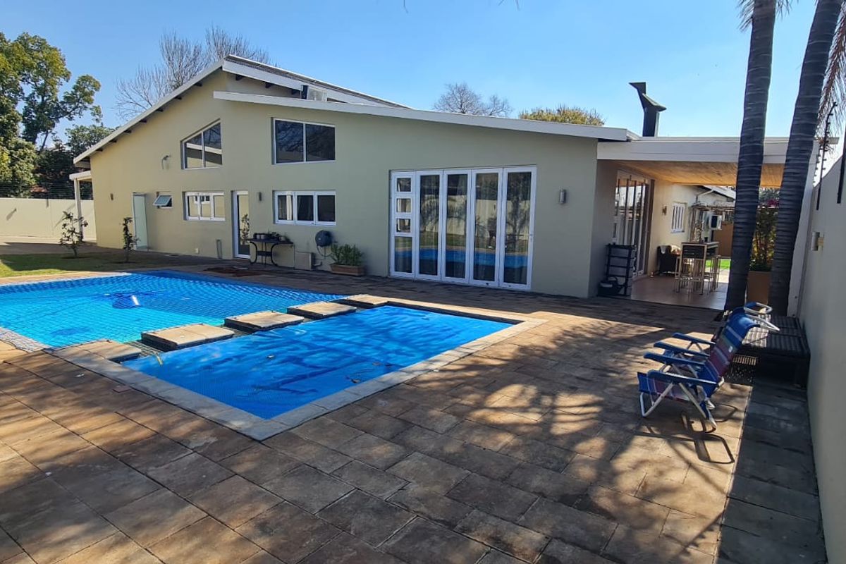 Rear exterior view featuring a swimming pool with a safety cover, paved patio area, and covered outdoor entertainment space with bi-fold doors.