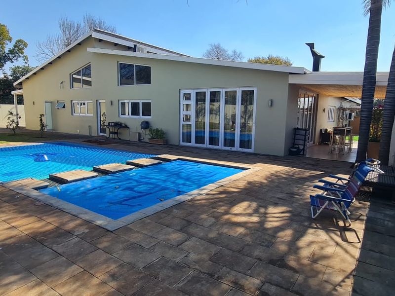 Rear exterior view featuring a swimming pool with a safety cover, paved patio area, and covered outdoor entertainment space with bi-fold doors.