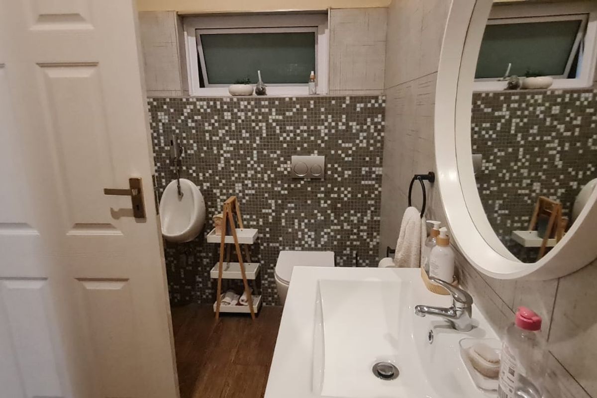 A compact bathroom featuring a wall-mounted urinal, wall-hung toilet, and a modern vanity basin with mosaic tile accents.