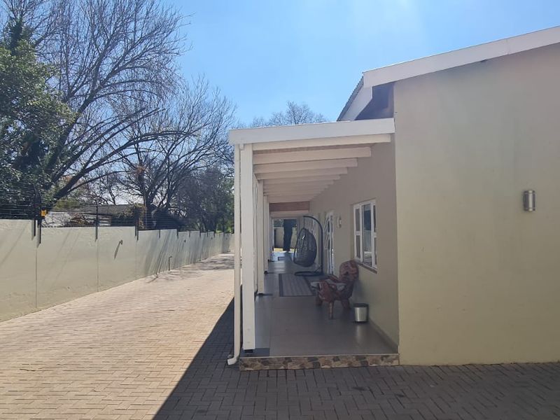 A view of the rear exterior featuring a paved driveway, perimeter wall with electric fencing, and a covered patio area.