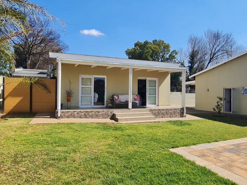Rear view of the property featuring a covered patio with stone detailing, sliding glass doors, and a well-maintained garden with a swimming pool.