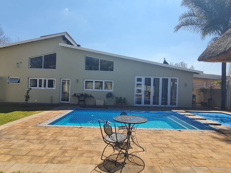 Rear exterior view featuring a swimming pool, paved patio area, and a thatched lapa, set against a modern home with raked roofline.