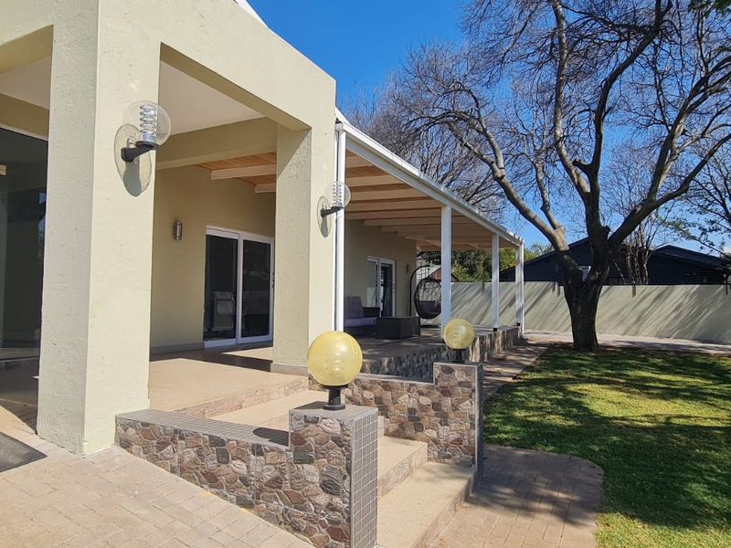 A spacious covered rear patio featuring stone-clad accents, paved flooring, and direct access to the garden through sliding glass doors.