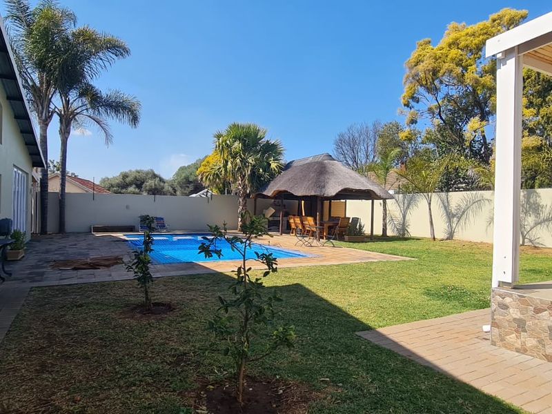 Spacious rear garden featuring a swimming pool, a thatched lapa entertainment area, and a covered patio with stone-clad pillars.