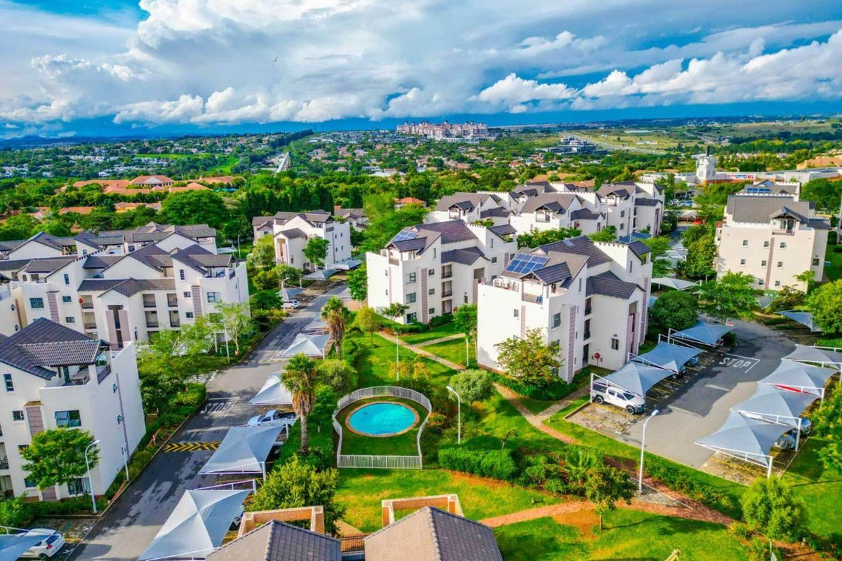 Aerial view of a residential apartment complex featuring landscaped gardens, a communal swimming pool, and covered parking bays.