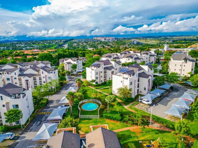 Aerial view of a residential apartment complex featuring landscaped gardens, a communal swimming pool, and covered parking bays.
