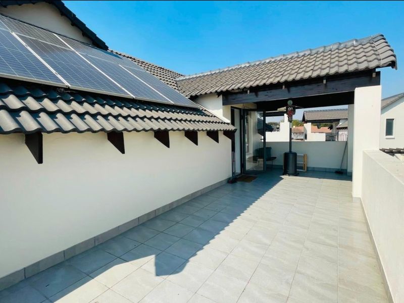 A spacious, tiled balcony featuring a covered section and integrated solar panels on the roof structure.