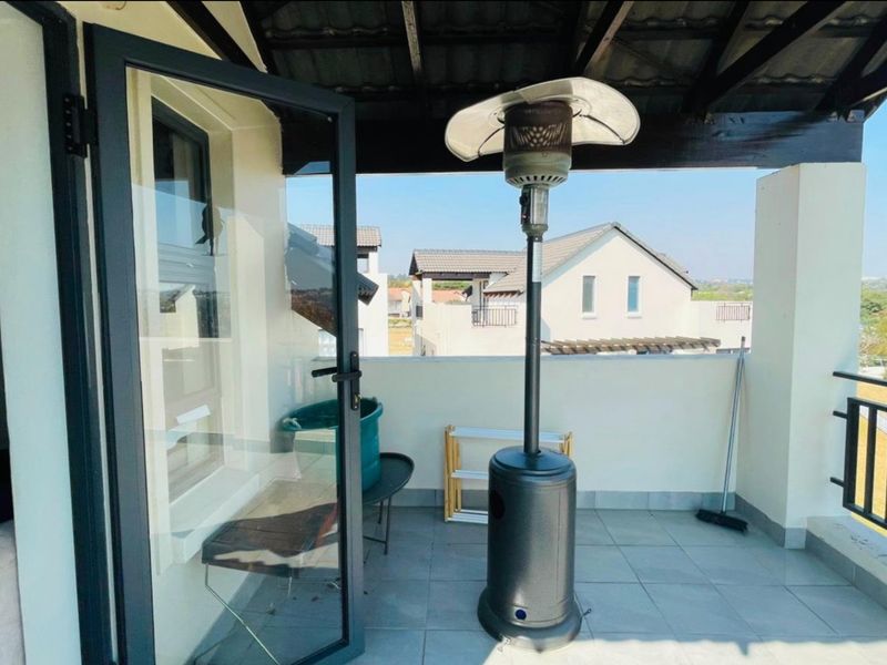 A covered balcony featuring tiled flooring and a metal balustrade, offering an open outdoor space accessible through a glass door.
