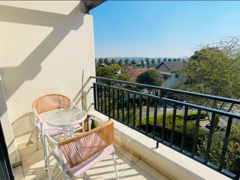 A private balcony featuring a metal balustrade and tiled flooring, offering elevated views of the surrounding neighborhood and greenery.