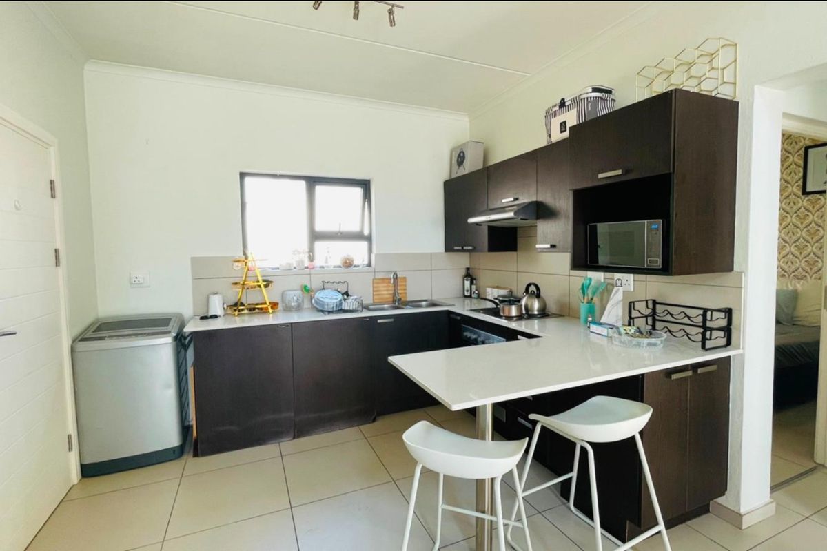 A functional kitchen featuring dark wood cabinetry, white stone countertops, a breakfast bar, and integrated appliances with tiled flooring.