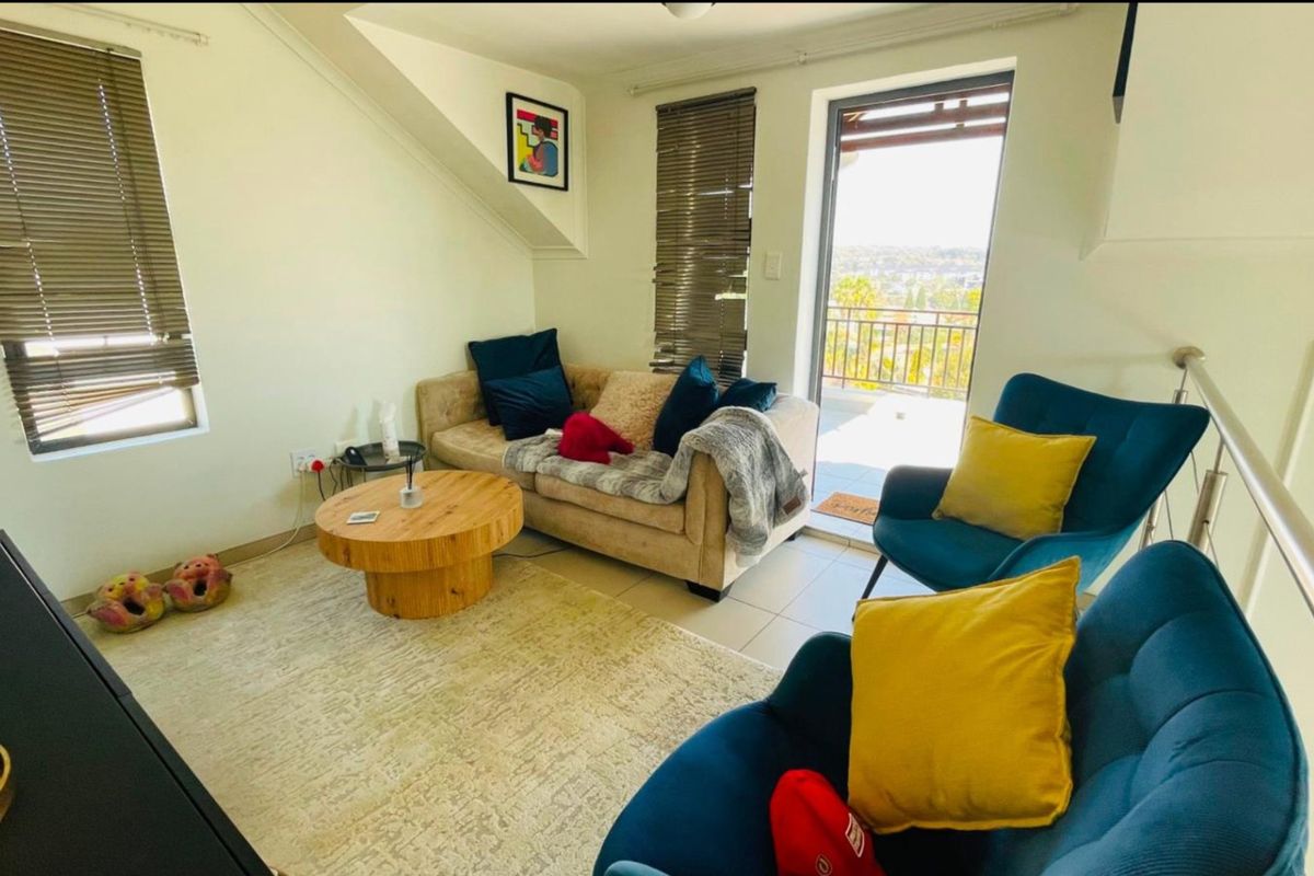 A bright living room featuring tiled floors, sloped ceilings, and direct access to a balcony with scenic views.