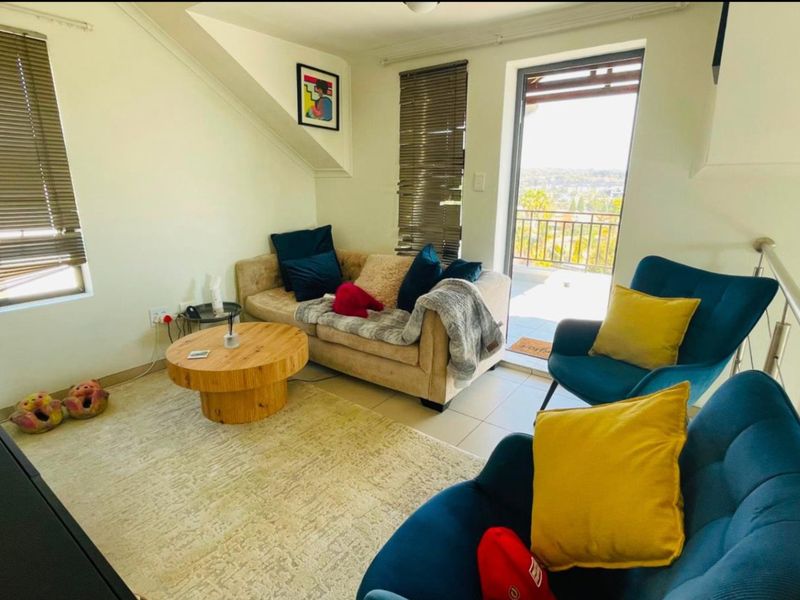 A bright living room featuring tiled floors, sloped ceilings, and direct access to a balcony with scenic views.