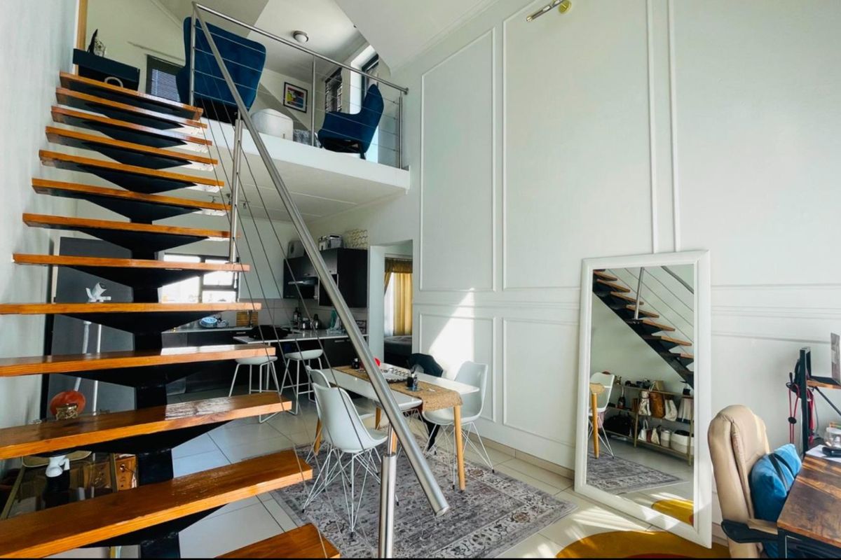 Open-plan living area featuring a modern floating staircase with stainless steel balustrades, wainscoting wall detailing, and a mezzanine level overlooking the main space.