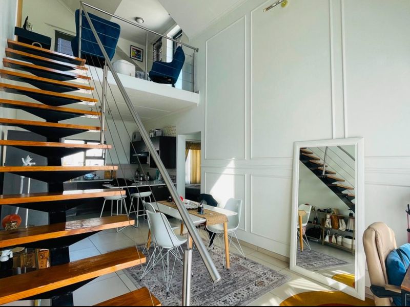Open-plan living area featuring a modern floating staircase with stainless steel balustrades, wainscoting wall detailing, and a mezzanine level overlooking the main space.