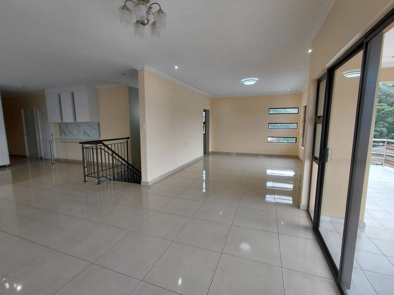 Spacious open-plan living area featuring neutral tiled floors, recessed lighting, and direct access to a balcony through large sliding glass doors.