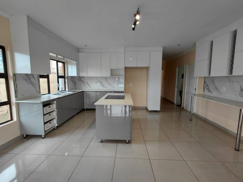 Modern, spacious kitchen featuring sleek grey and white cabinetry, a central island with a built-in hob, marble-look backsplash, and polished tiled flooring.