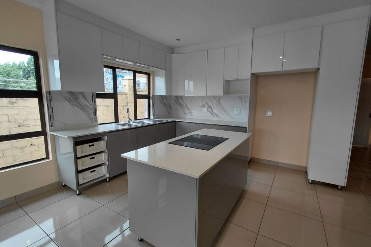 Modern kitchen featuring sleek white and grey cabinetry, stone countertops, a central island with an integrated hob, and large format floor tiles.