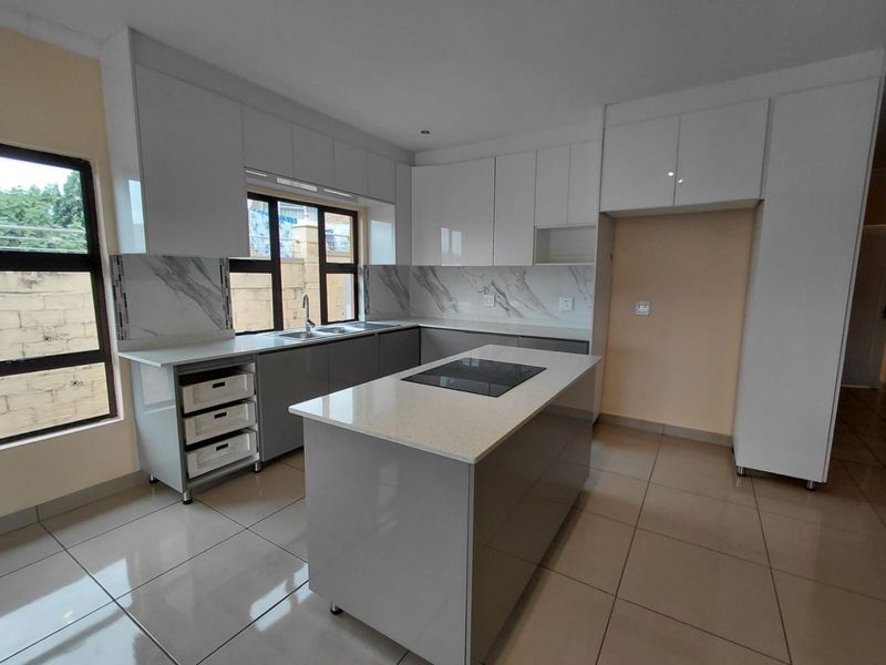 Modern kitchen featuring sleek white and grey cabinetry, stone countertops, a central island with an integrated hob, and large format floor tiles.