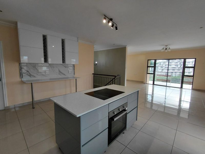 Spacious open-plan kitchen and living area featuring a modern island with built-in oven, sleek cabinetry, and large sliding doors leading to a balcony.