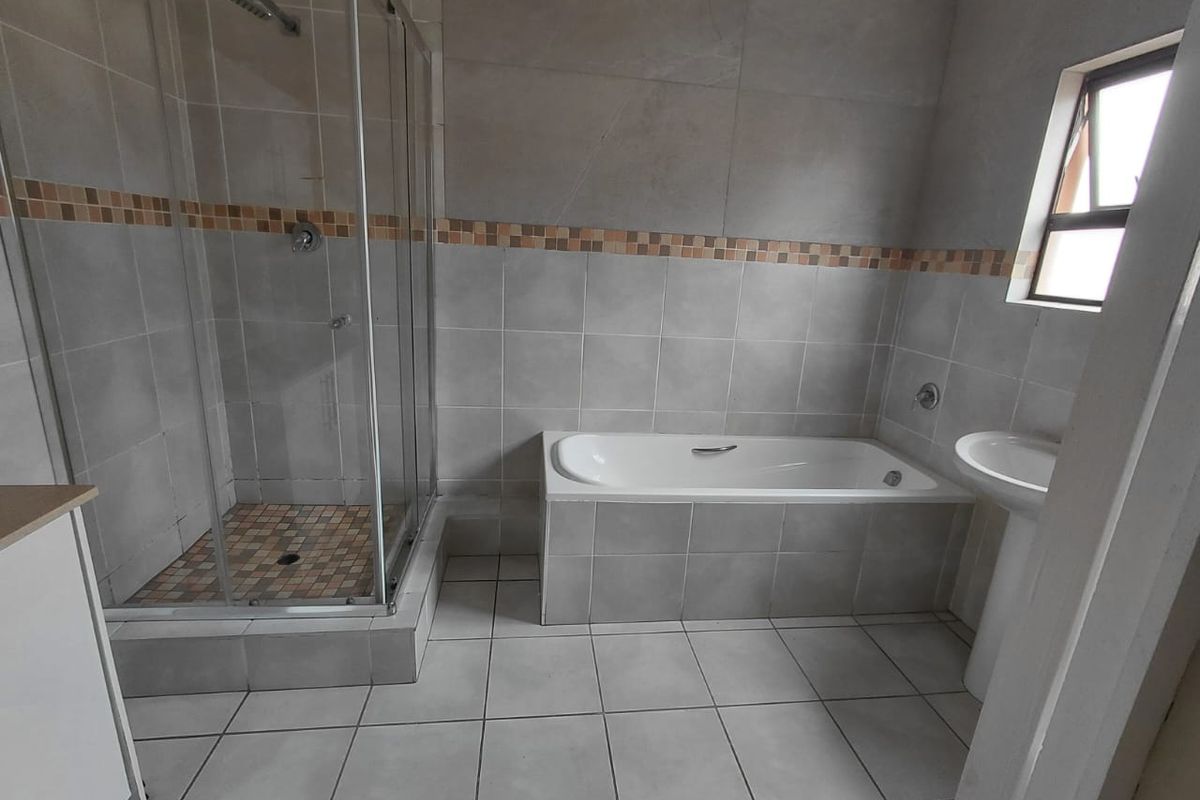 A functional bathroom featuring a separate shower enclosure, a built-in bathtub, and a pedestal basin with neutral wall and floor tiling.