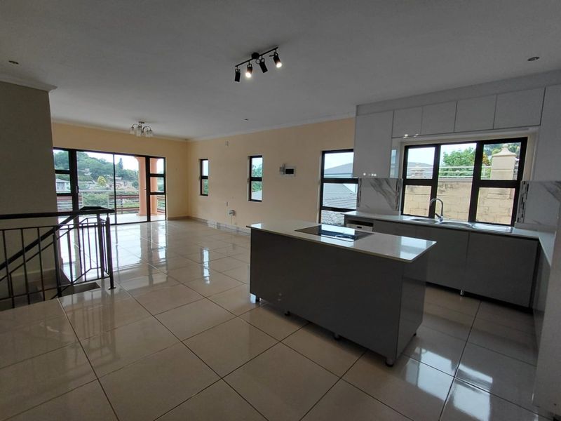 Spacious open-plan living and kitchen area featuring modern cabinetry, a central island with a hob, tiled floors, and access to a balcony.
