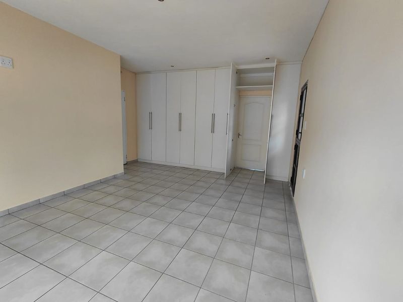 An empty bedroom featuring neutral tiled flooring, built-in white cupboards, and recessed ceiling lighting.