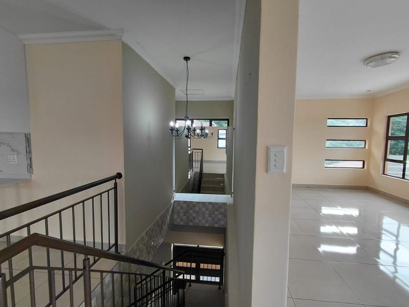 A bright, tiled hallway and staircase area featuring metal balustrades, neutral wall tones, and modern light fixtures in a clean, open-plan townhouse layout.