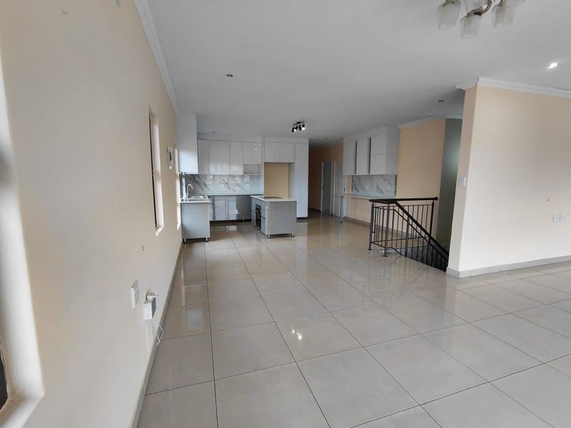 Spacious open-plan living area featuring modern kitchen cabinetry, a central island, marble-look splashbacks, and polished floor tiles with an adjacent staircase.