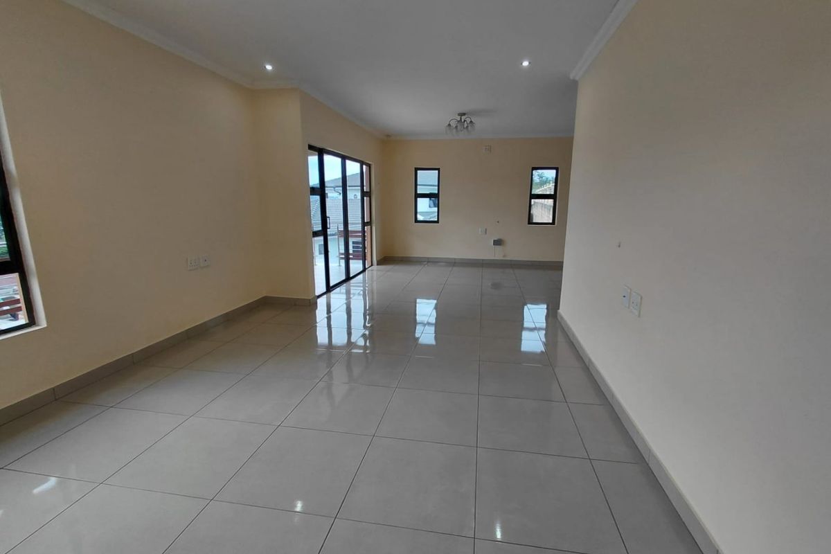 A spacious, empty living area featuring neutral walls, polished porcelain floor tiles, and large aluminium-framed windows and sliding doors providing ample natural light.