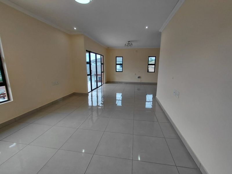 A spacious, empty living area featuring neutral walls, polished porcelain floor tiles, and large aluminium-framed windows and sliding doors providing ample natural light.