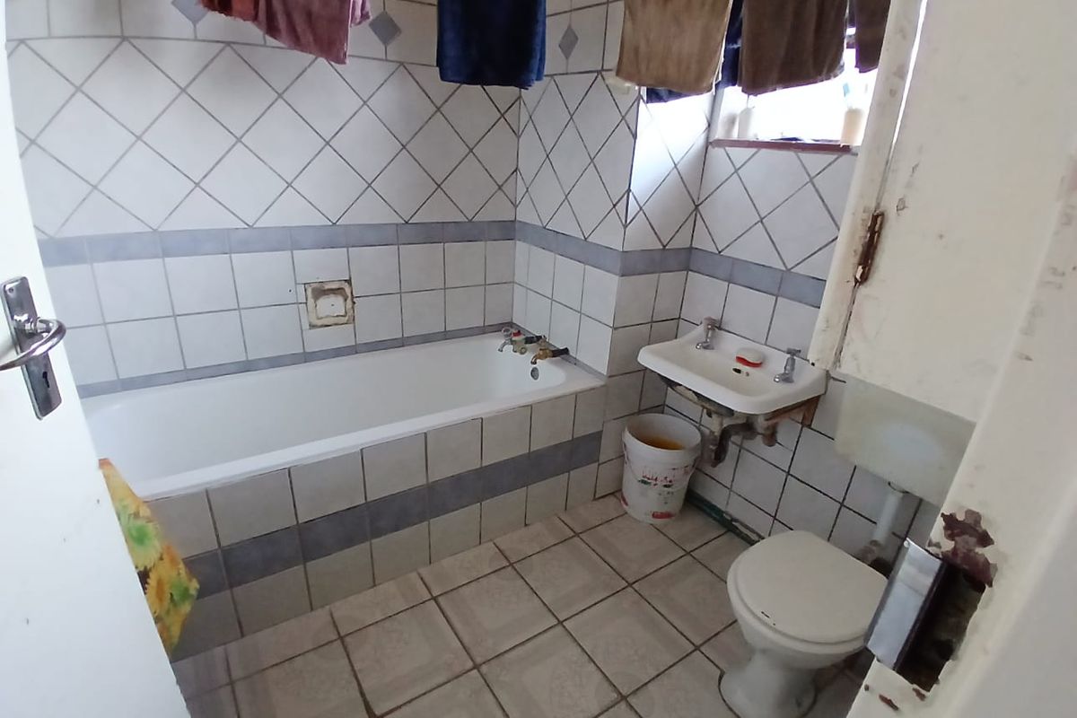 A dated bathroom featuring a standard bathtub, wall-mounted basin, and toilet with original ceramic tiling throughout.