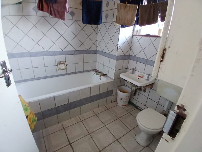 A dated bathroom featuring a standard bathtub, wall-mounted basin, and toilet with original ceramic tiling throughout.