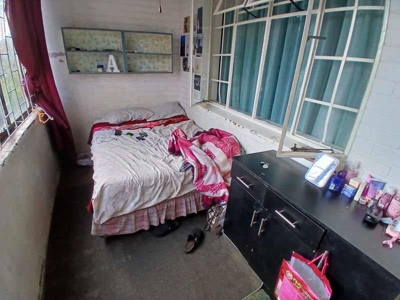 A compact bedroom featuring painted brick walls, built-in shelving, and large steel-framed windows providing natural light.