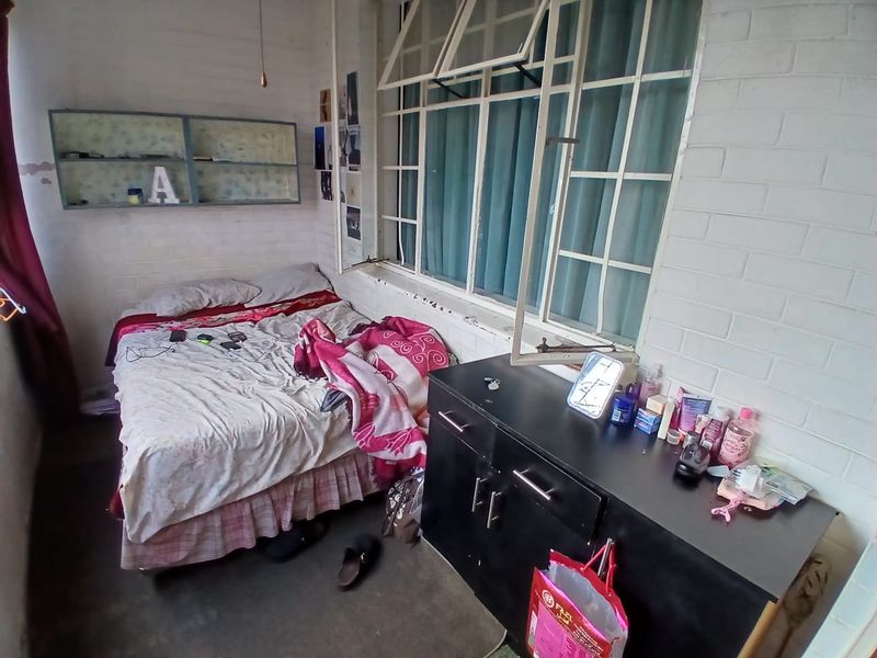 A bedroom featuring a large steel-framed window and built-in wall shelving, requiring cosmetic updates to the wall finishes.