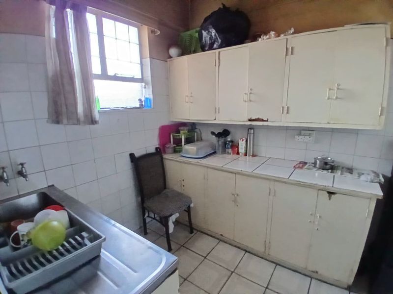 A dated kitchen featuring original built-in cabinetry, tiled countertops, and a stainless steel sink, offering significant potential for modernization and renovation.