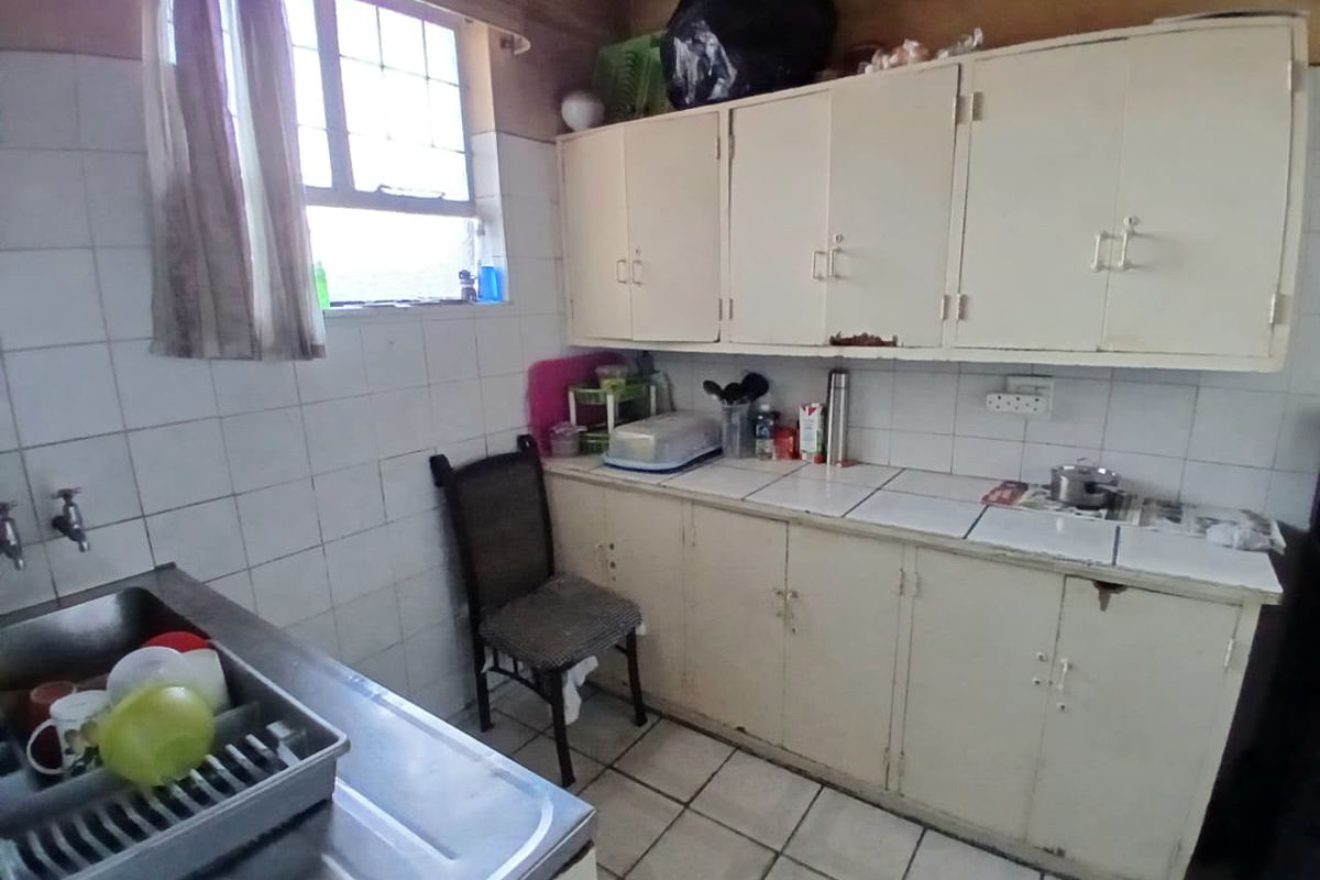 A dated kitchen featuring original built-in cabinetry, tiled countertops, and tiled flooring, offering significant potential for modernization and renovation.