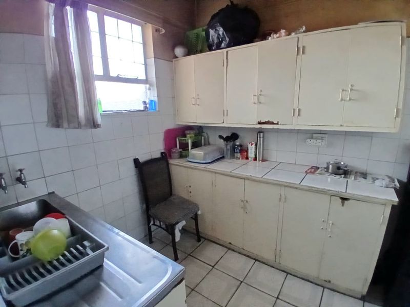 A dated kitchen featuring original built-in cabinetry, tiled countertops, and tiled flooring, offering significant potential for modernization and renovation.