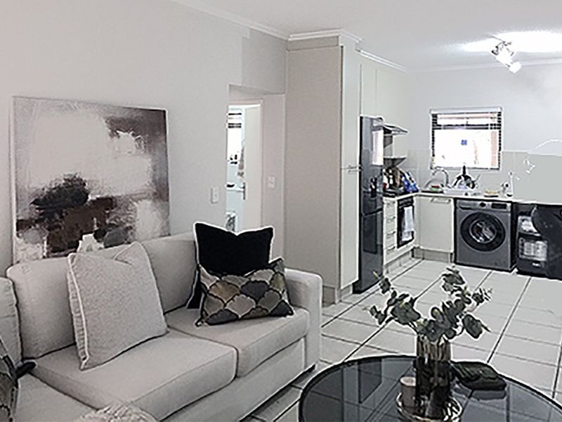Open-plan living area featuring a functional kitchen with built-in cabinetry, tiled flooring, and integrated appliances, seamlessly connected to the main living space.